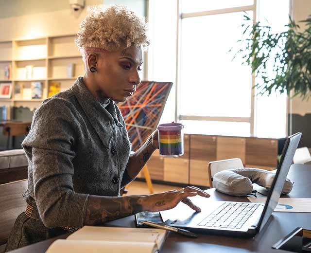 A person holding a coffee cup while typing on a laptop.